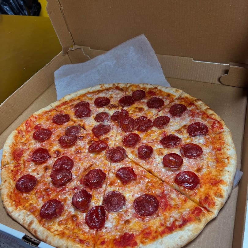 A whole pepperoni pizza, sliced, sits in an open cardboard delivery box.