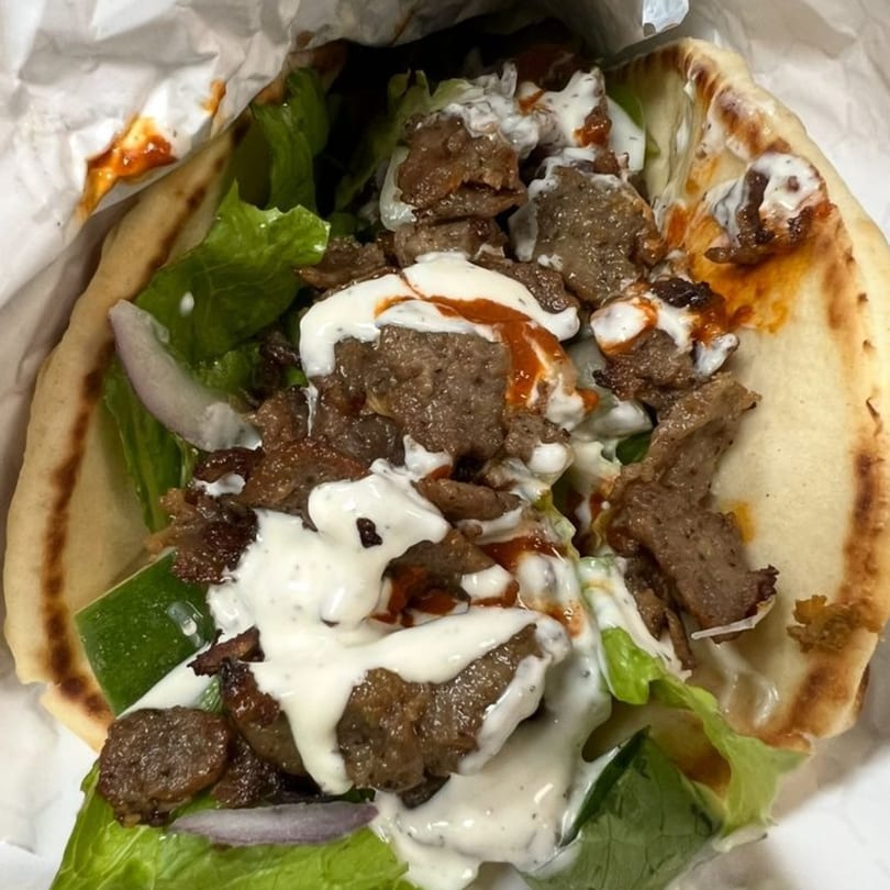 A close-up of a gyro with meat, lettuce, onions, and white and red sauces in pita bread.