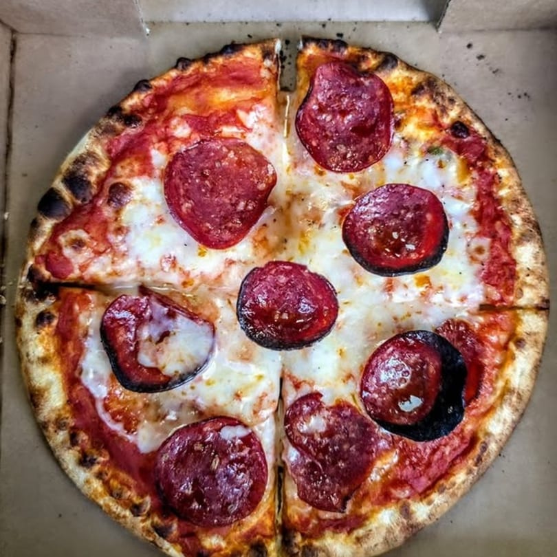 A whole pepperoni pizza with a crispy crust, cut into four slices, in a cardboard box.