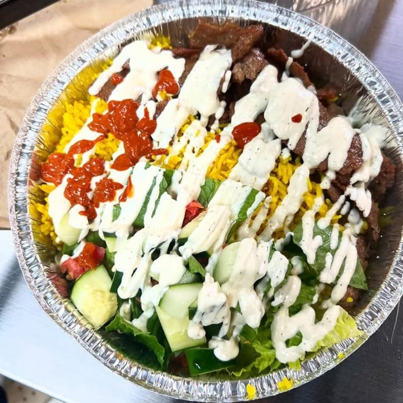 A gyro platter with yellow rice, meat, lettuce, cucumbers, tomatoes, white sauce, and red sauce.