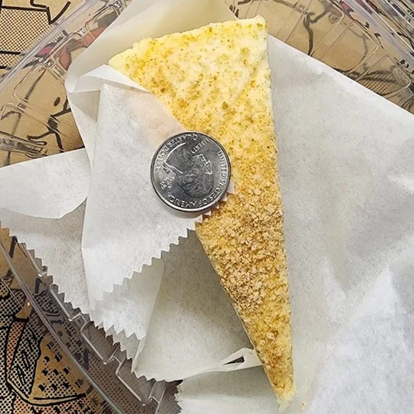 A slice of NY Pizza & Gyro Inc's pizza with a quarter on top for scale, in a plastic container.